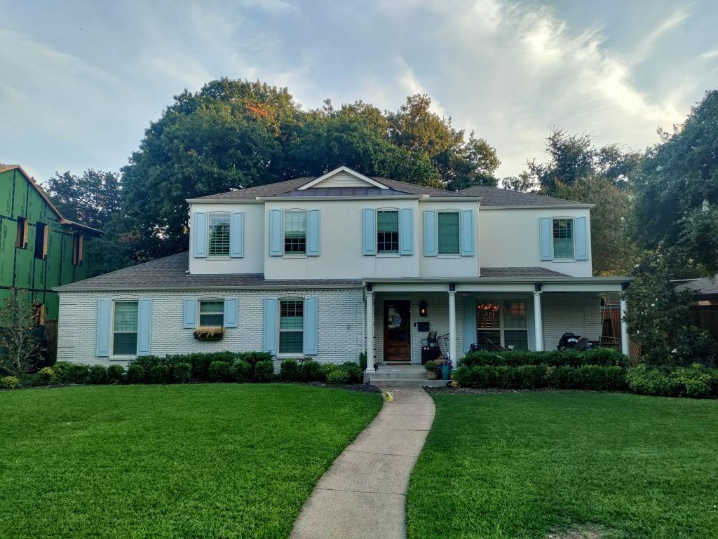 Two-story white house with light blue shutters, a green lawn, and a walkway leading to the front door.