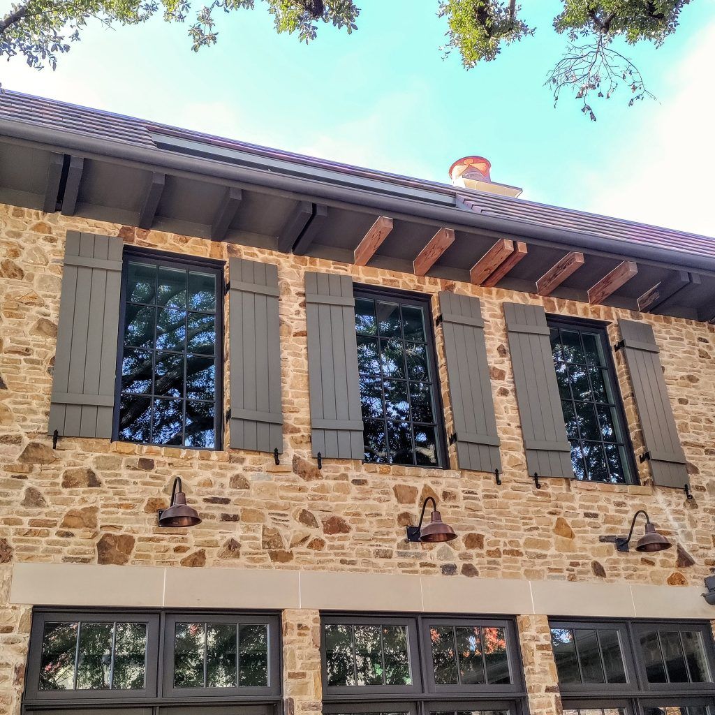 Stone building with dark-framed windows and shutters. Overhanging roof with wooden beams.