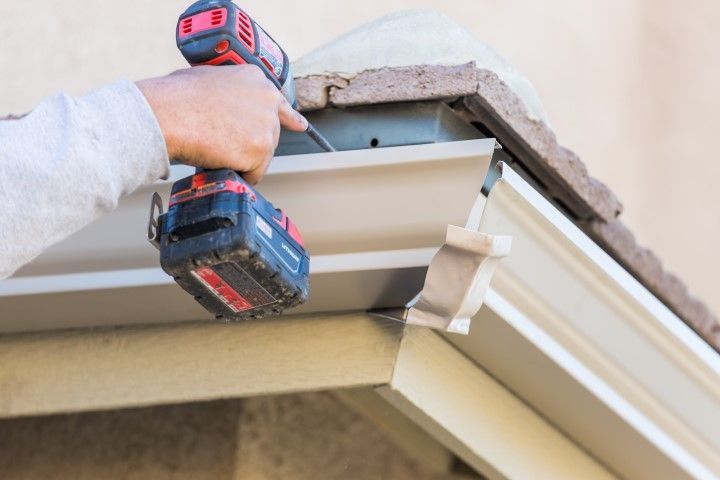 Hands using a cordless drill to install gutter trim on a house roofline