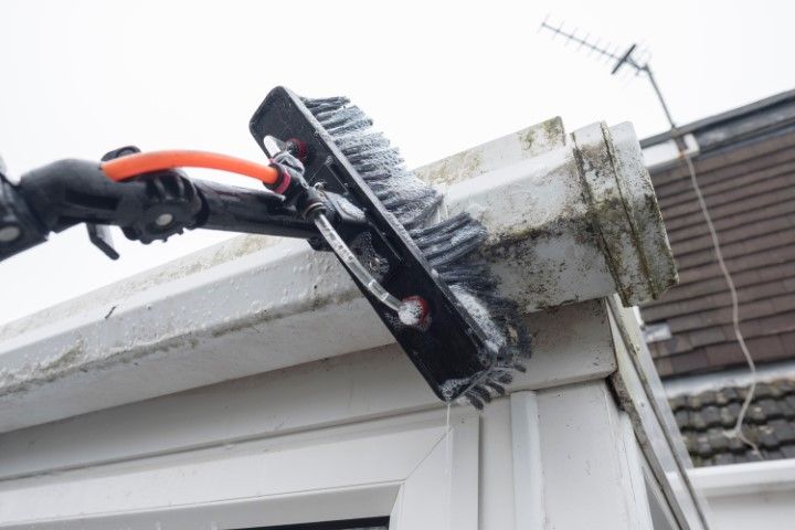 Gloved hand cleaning a house gutter with a brush on a roofline