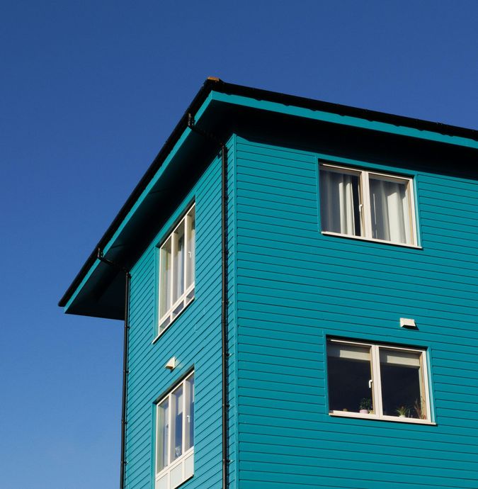 Teal house exterior with white-trimmed windows against a clear blue sky