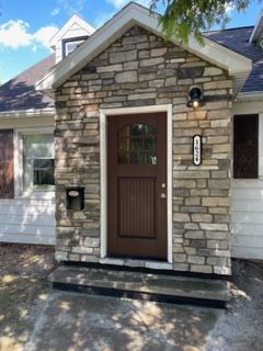 The front door of a house with a stone wall and a brown door.