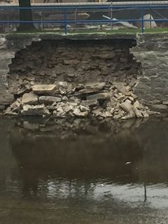 A retention wall with rocks falling into a river.