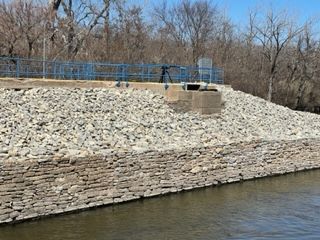 A large pile of rocks and a stone wall is sitting next to a body of water.