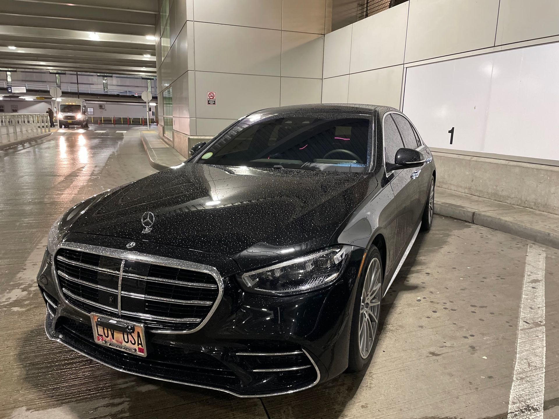 Black Mercedes sedan parked in a covered parking garage. The car has a personalized license plate.