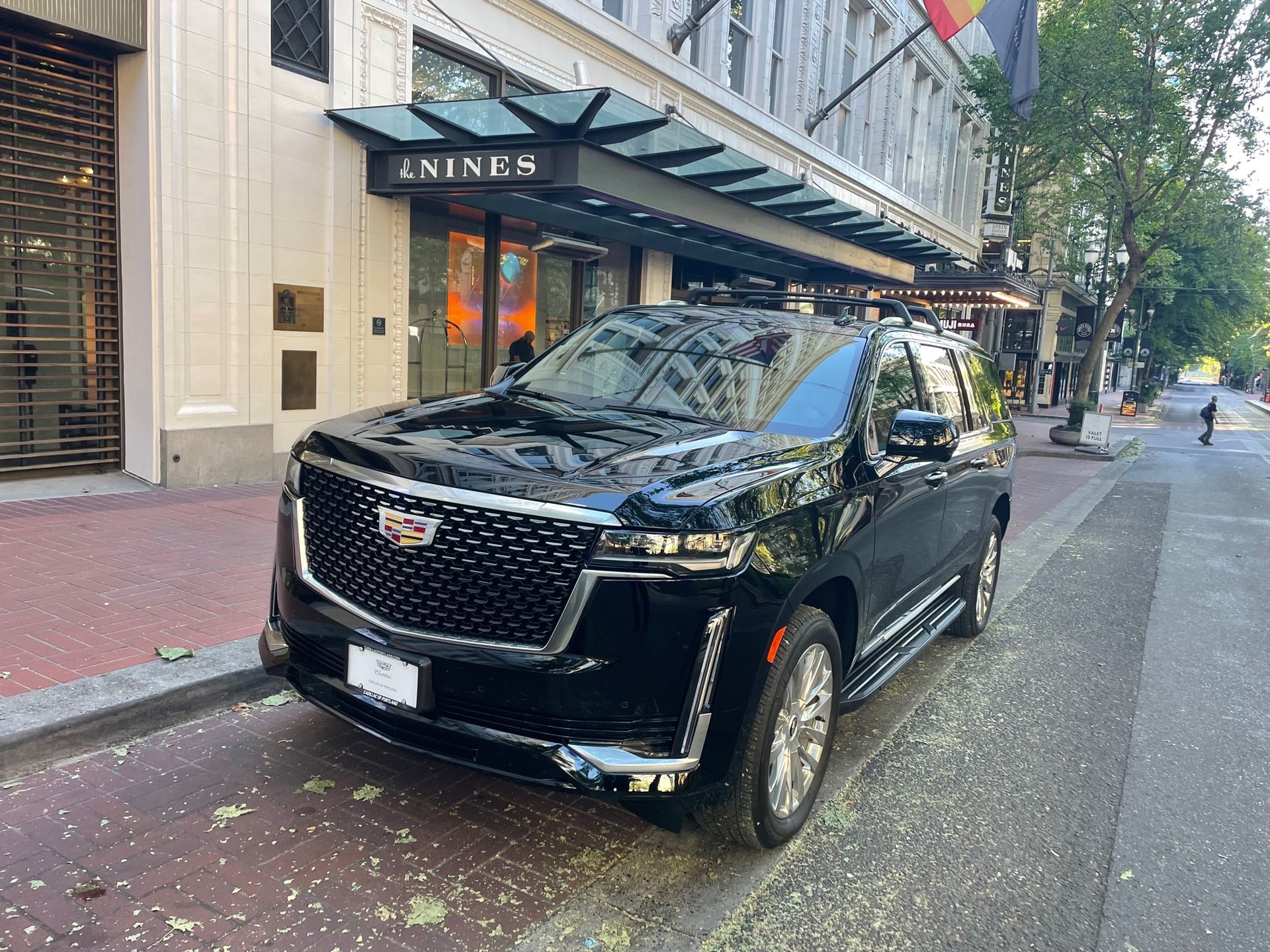 Black Cadillac Escalade parked in front of the Hotel Monaco entrance in Portland, Oregon. The vehicle is parked on a brick street.