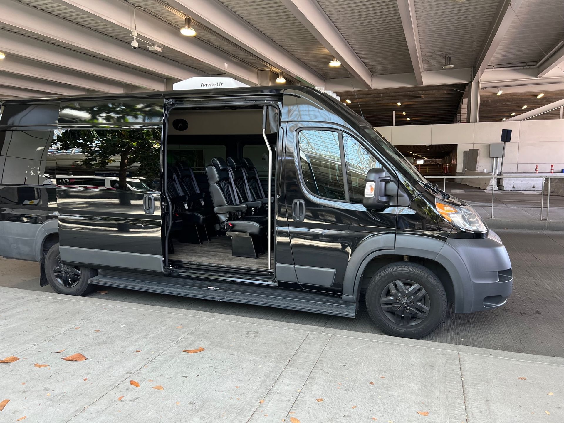 Black passenger van parked with its sliding door open under a covered area. Seats are visible inside the van.