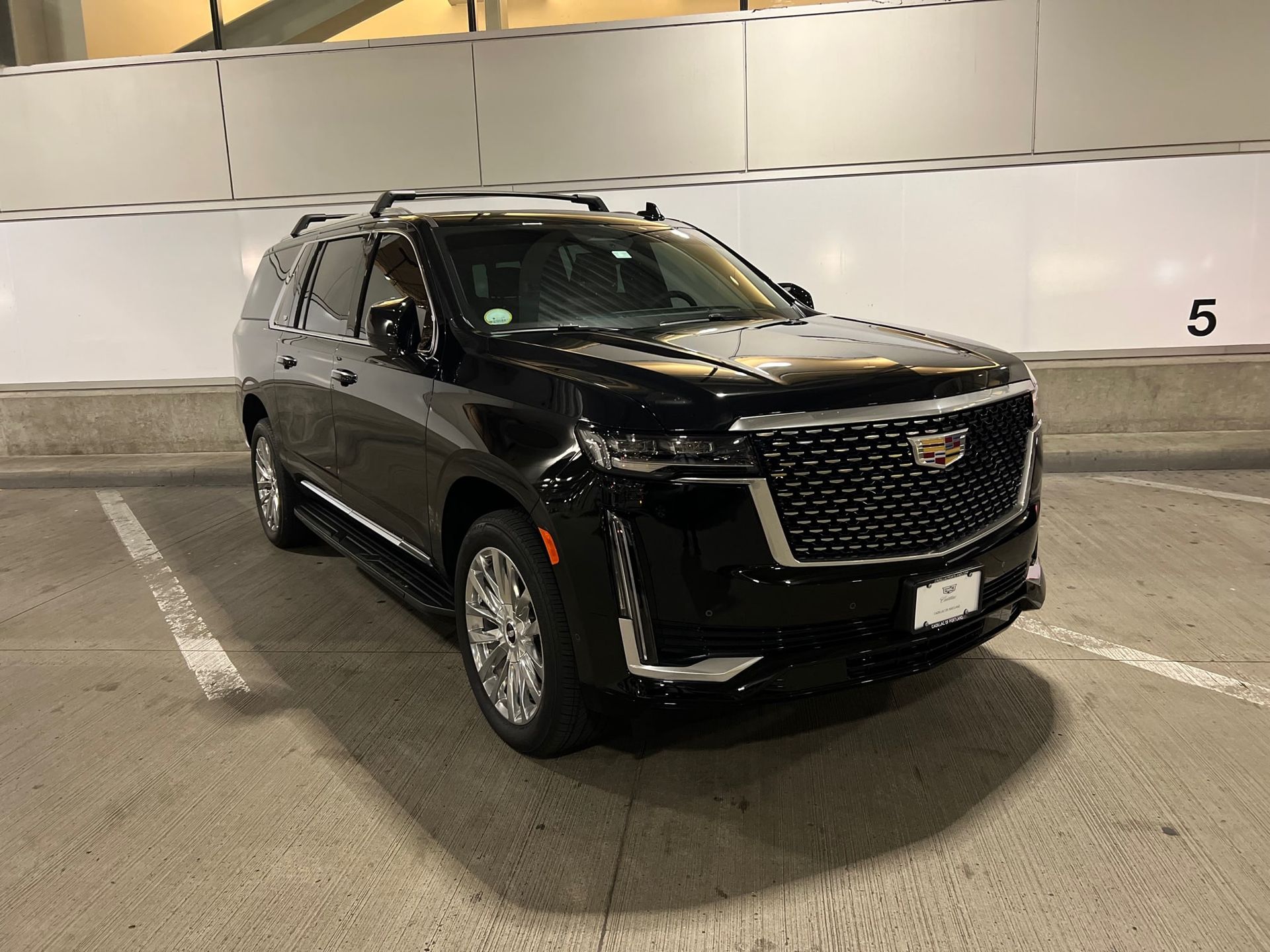 Black Cadillac Escalade SUV parked in a parking garage. The car is facing forward, with its front visible.