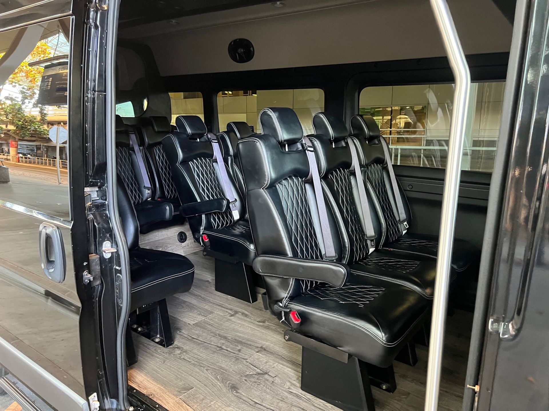 Black passenger van interior with black and gray leather seats, light gray floor, and open door.