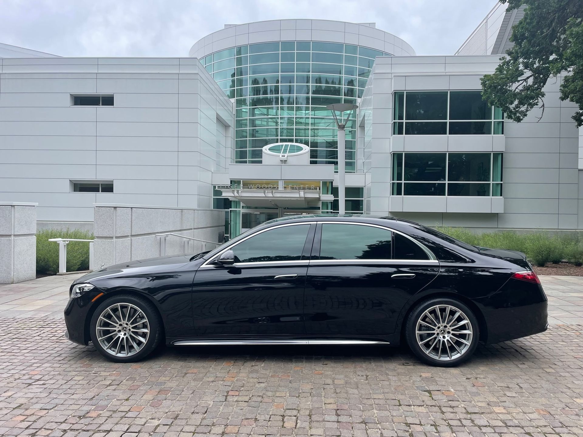 A black Mercedes-Benz sedan parked in front of a modern building with large glass windows and doors.