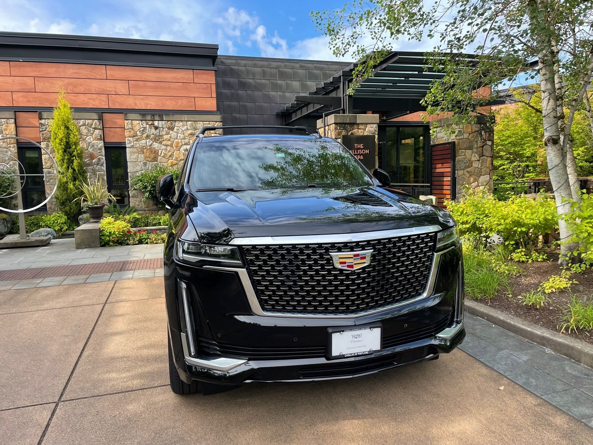 A black Cadillac Escalade parked in front of a stone and wood building on a sunny day.