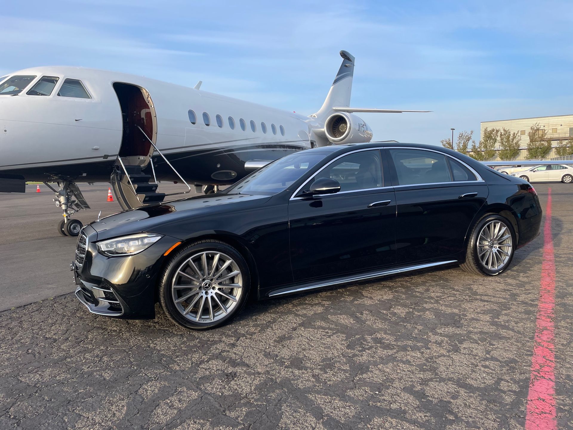Black Mercedes sedan parked on the tarmac next to a private jet, setting for a luxury travel scene.