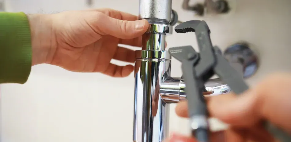 A person is fixing a pipe with a wrench.