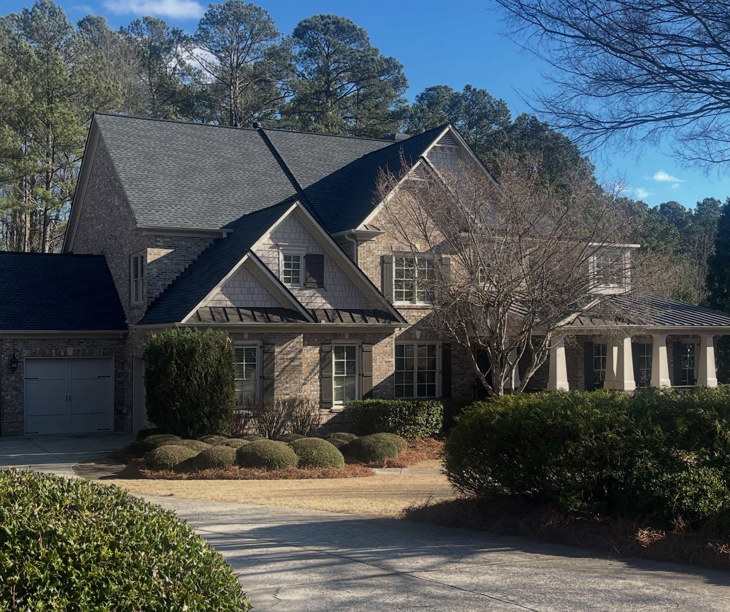 A large, two-story brick house with a dark gabled roof, surrounded by trees and a landscaped front yard with a driveway.