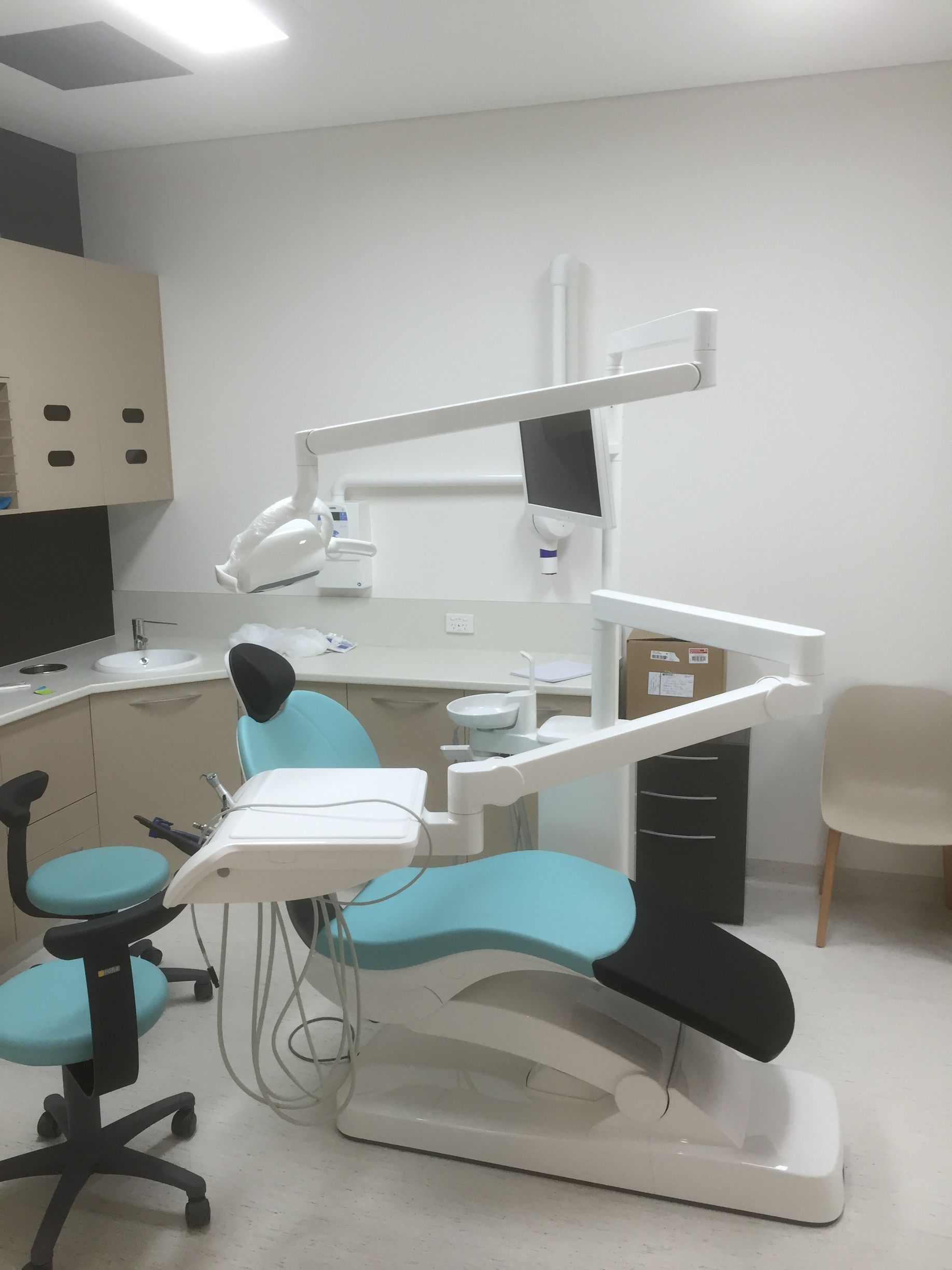 Dental chair in a light, modern room, with overhead light and instruments. Another chair to the left.