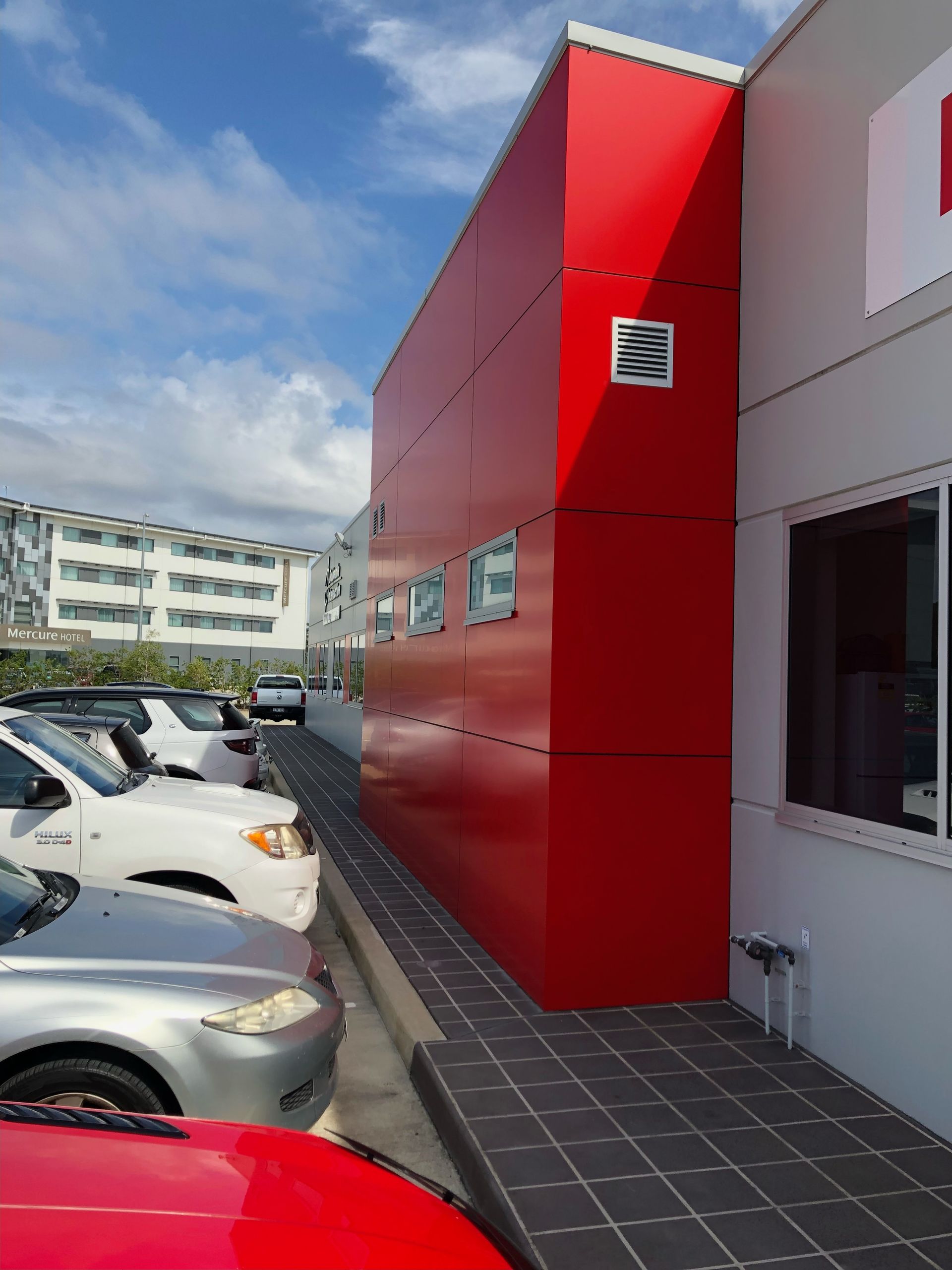 Red building facade next to a sidewalk with parked cars. Blue sky.