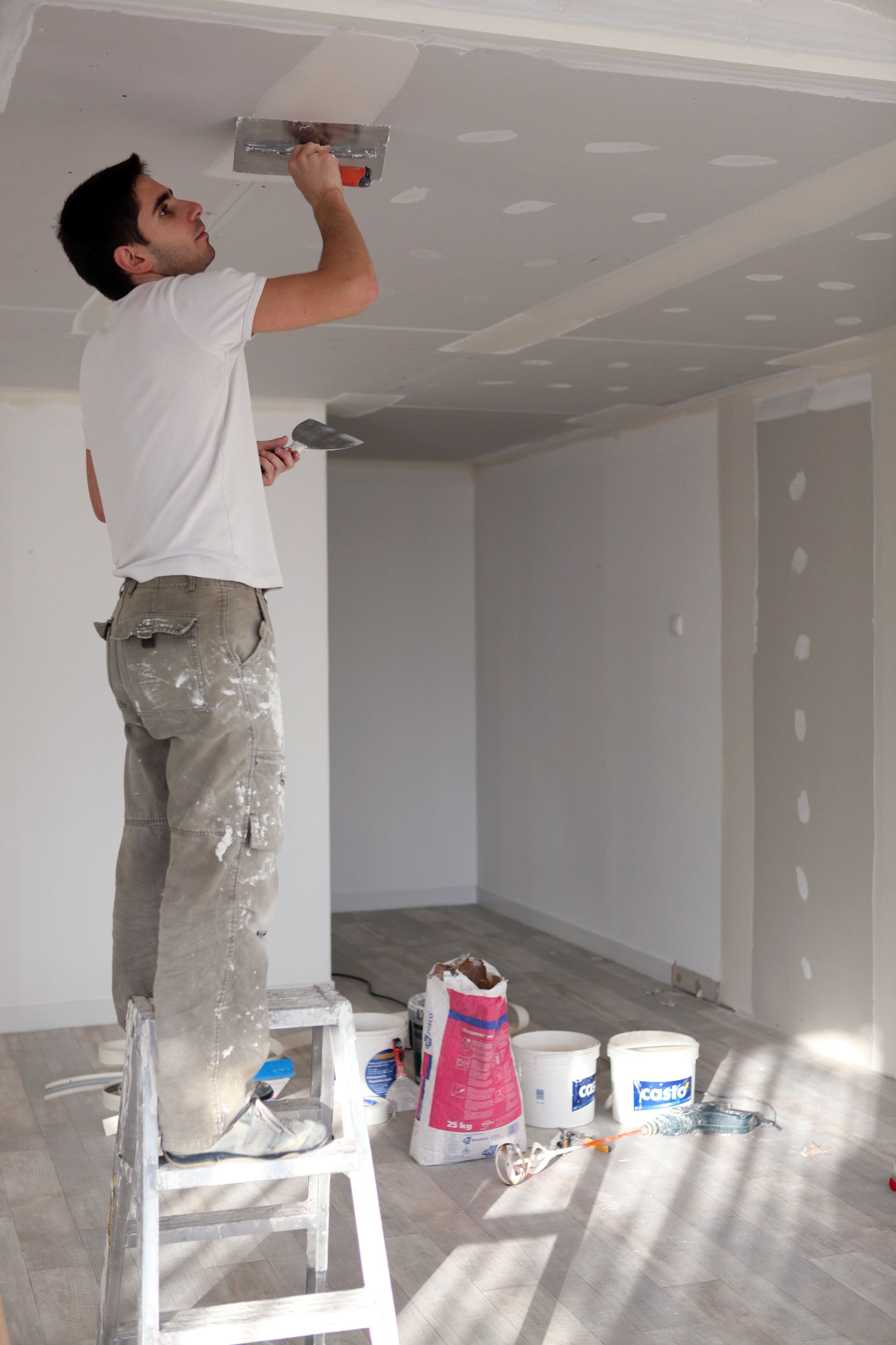 a man is standing on a ladder painting a ceiling .