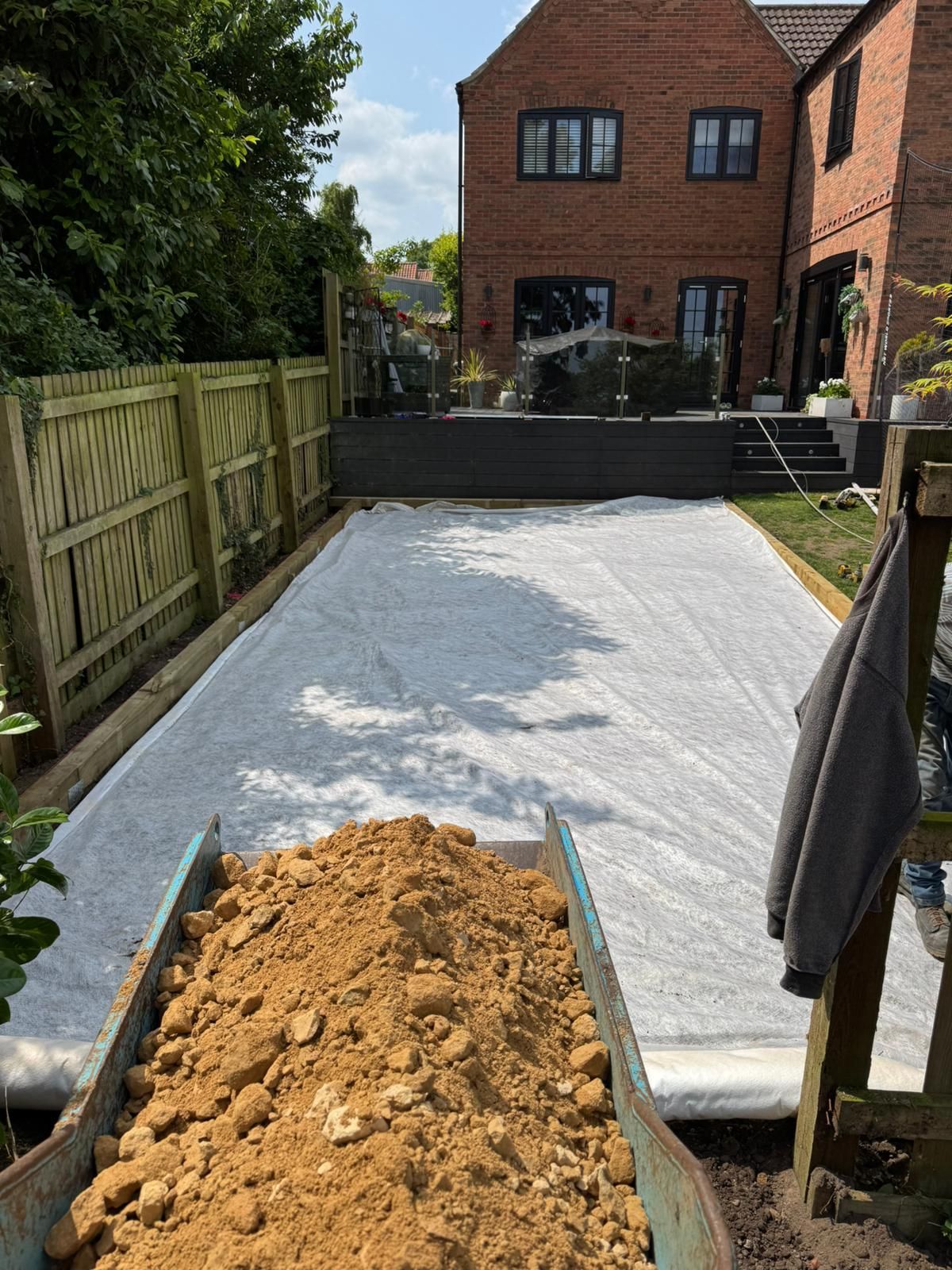 Wheelbarrow with dirt, next to a garden prepared for a project, with a house in the background.