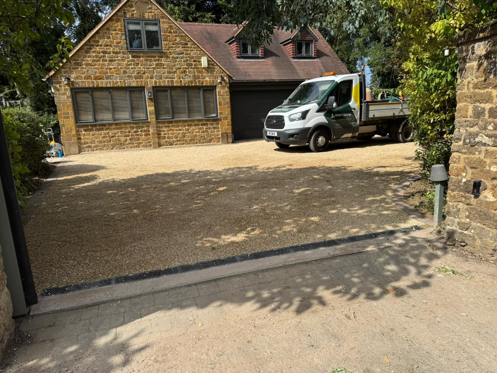 Gravel driveway with a truck parked in front of a stone building, under a sunny sky.