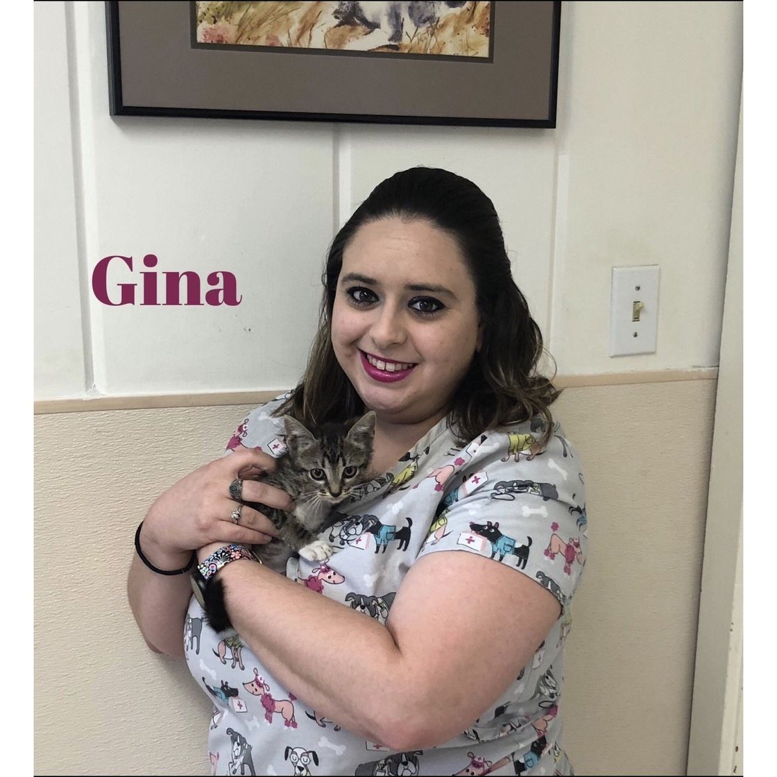 A woman in a scrub top is holding a cat in her arms.