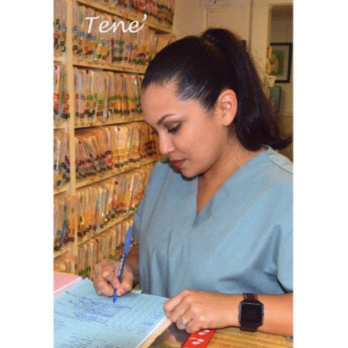 A woman in a blue scrub top is writing on a piece of paper
