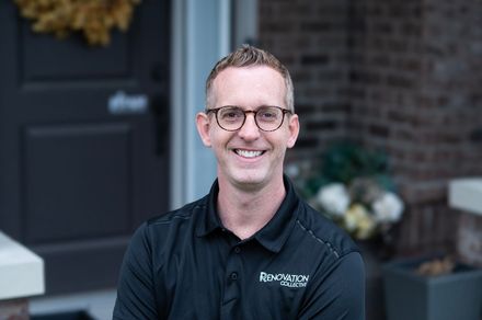 A man wearing glasses and a black shirt is standing in front of a door.