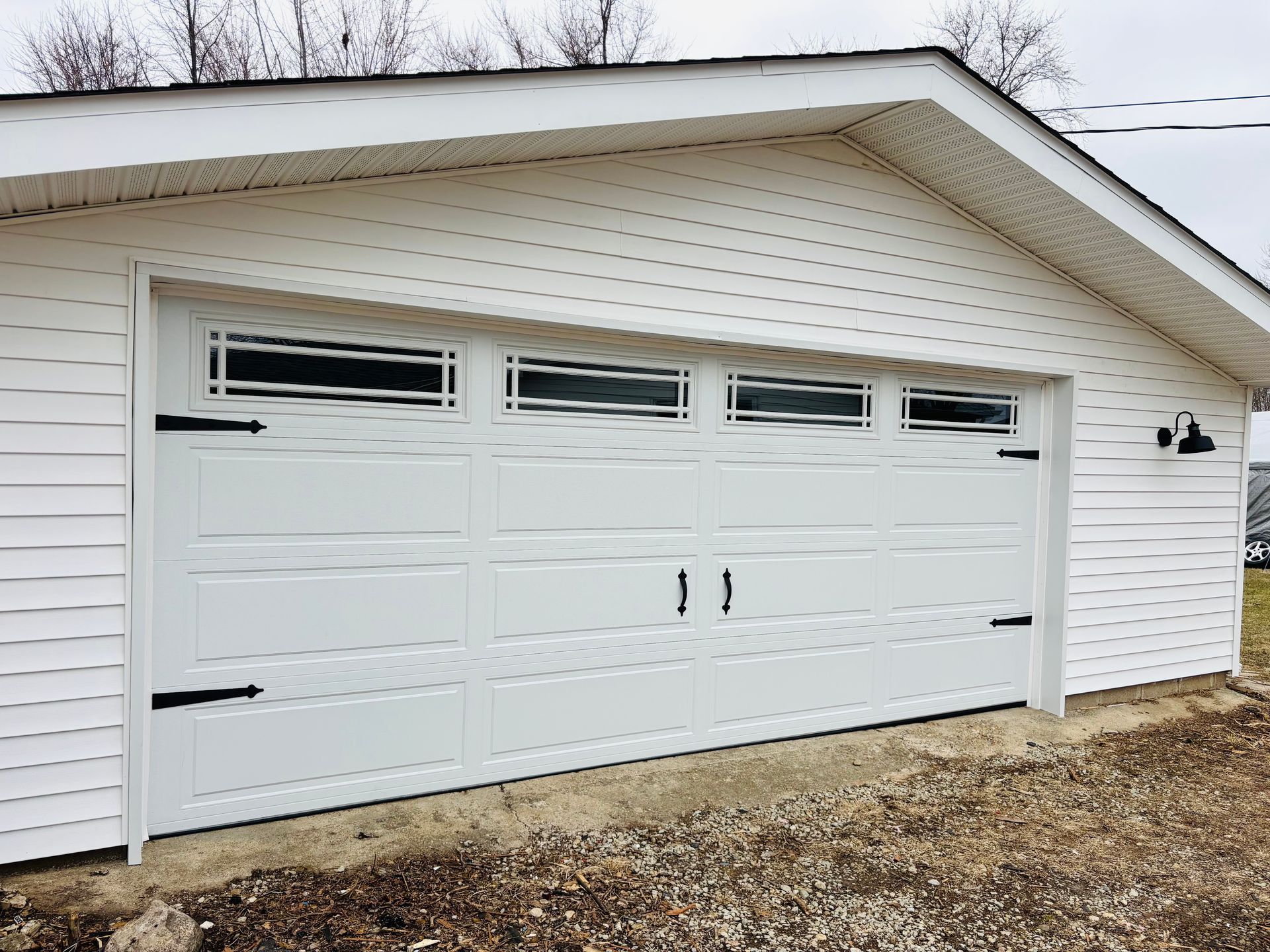 A white garage door with black handles is sitting on the side of a house.
