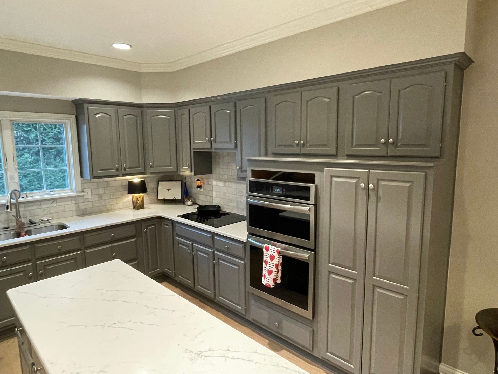 A kitchen with gray cabinets , white counter tops , and stainless steel appliances.