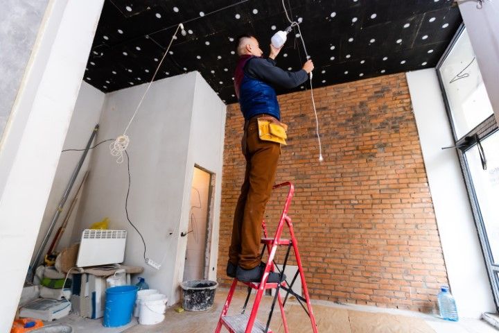 A man is standing on a ladder fixing a light bulb.