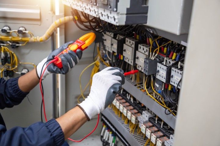 An electrician is working on an electrical box with a multimeter.