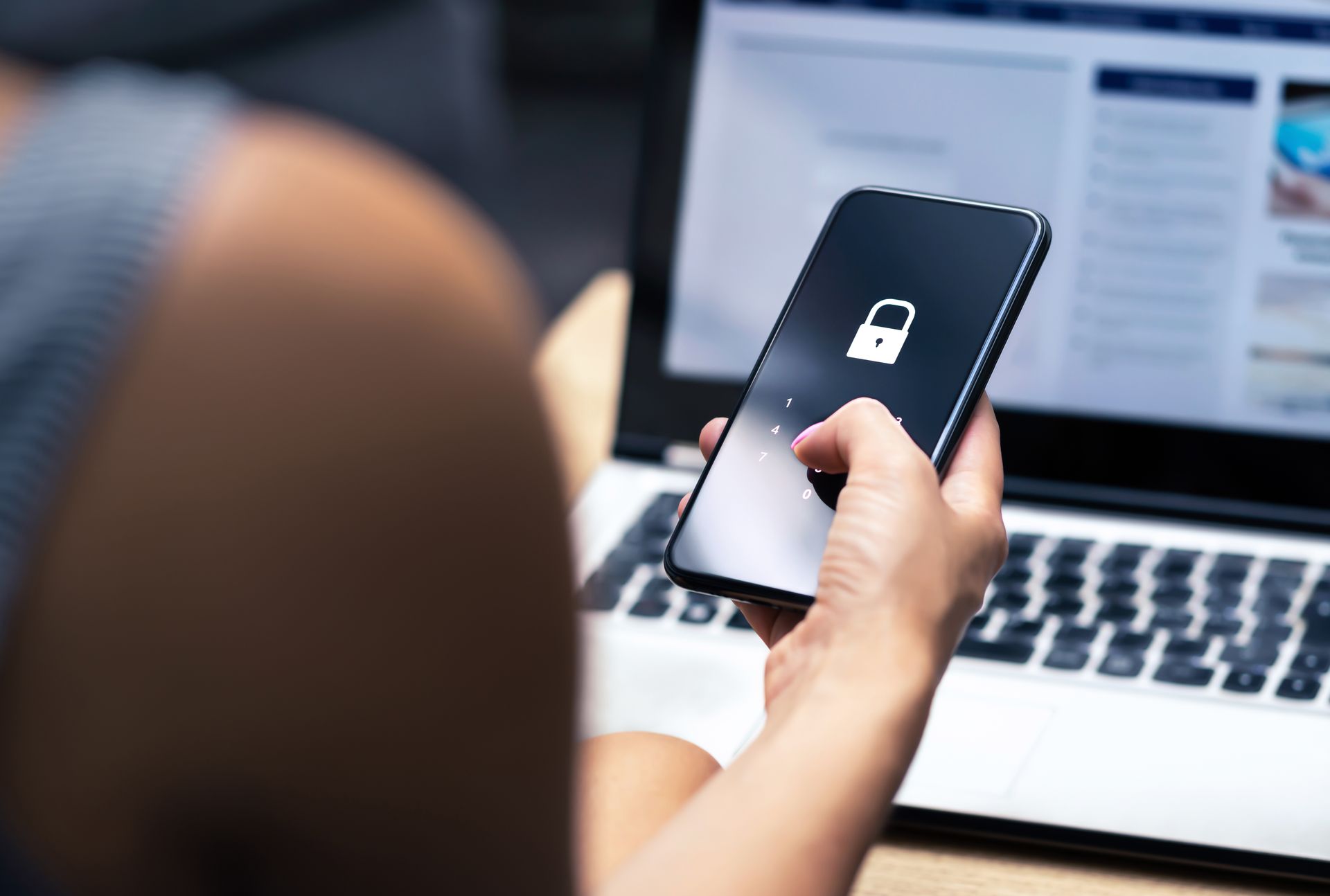 Person holding locked smartphone in front of a laptop.