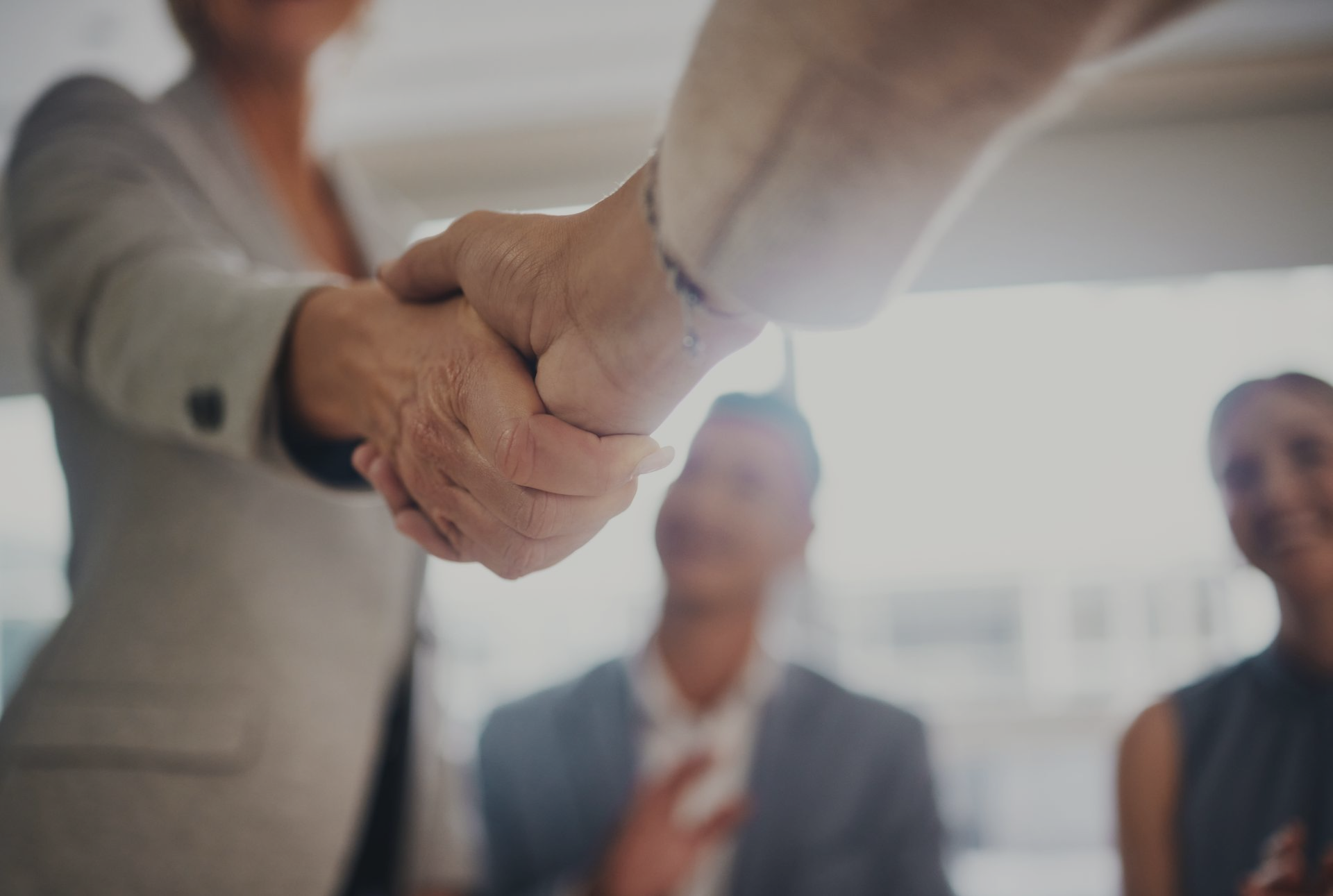 People shaking hands in an office, other colleagues in background.