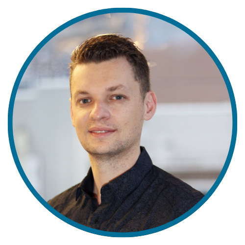 A man in a black suit and tie smiles, inside a teal circle.