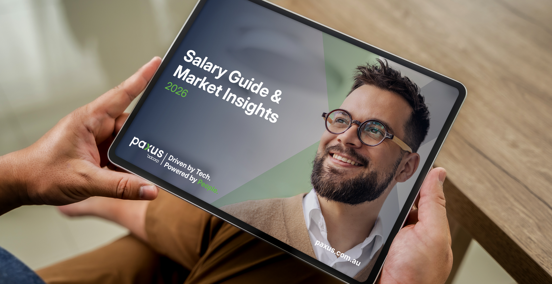 Person holding a tablet with a salary guide on the screen. The cover features a smiling person and the title