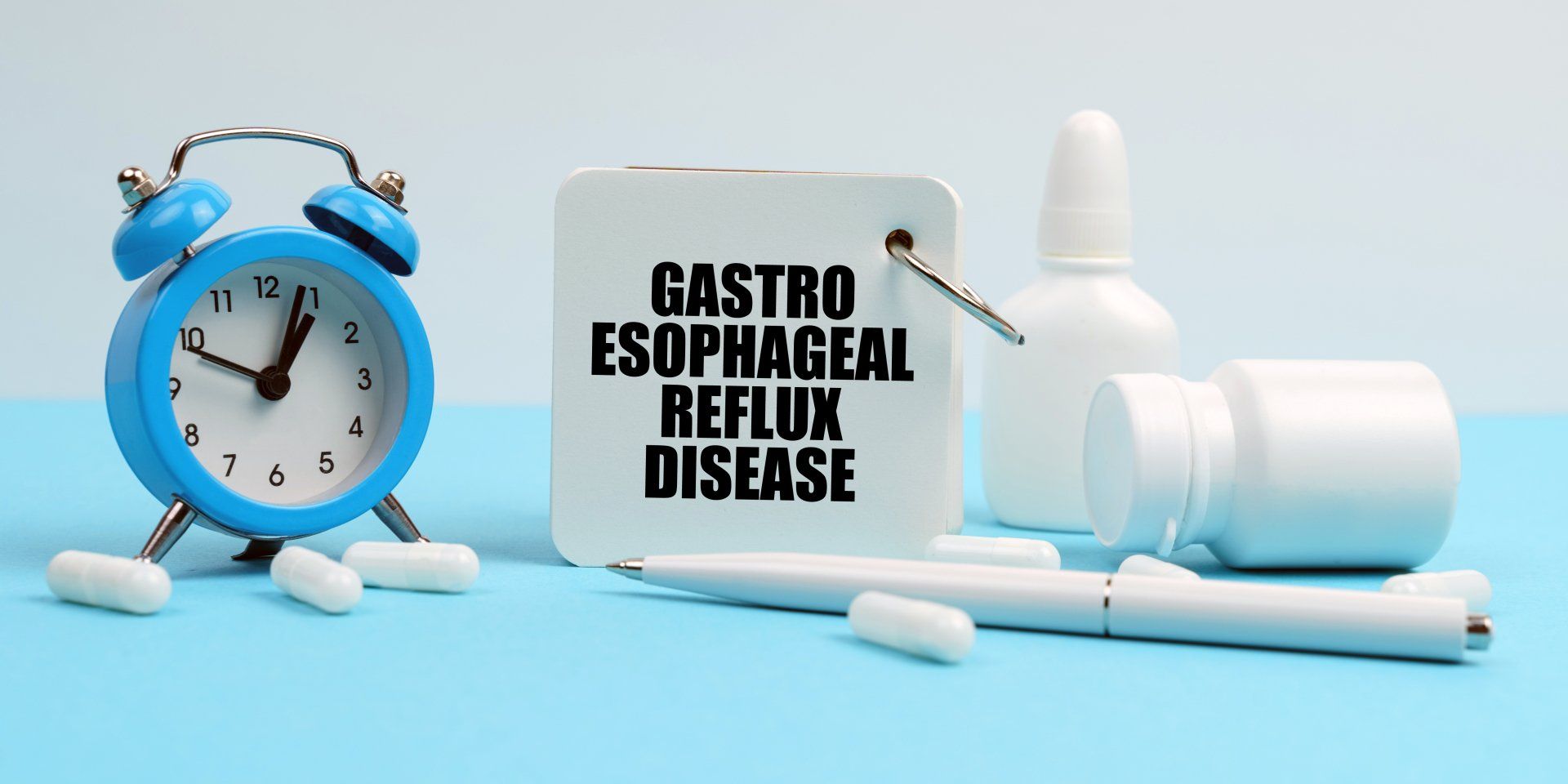 Clock, Sign that says Gastro Esophageal Reflux Disease, empty bottles, a pen and medicine sitting on a table.