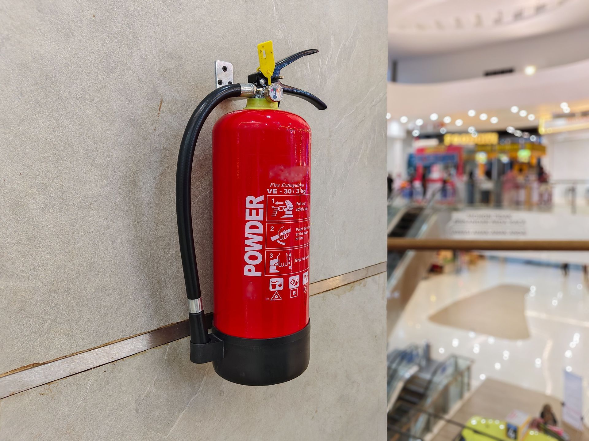 Red fire extinguisher mounted on a wall in a mall hallway. Red fire extinguisher mounted on a wall in a mall hallway.