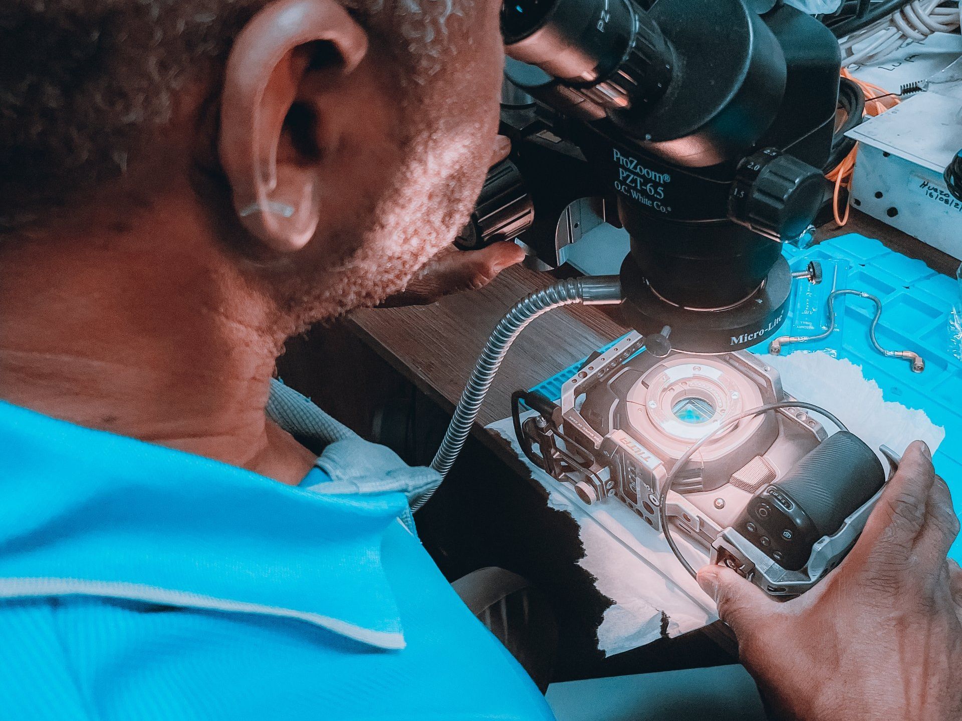 a man in a blue shirt is working on a camera under a microscope