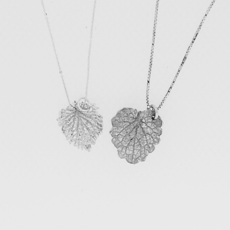 Two necklaces with leaves on them are on a white surface.