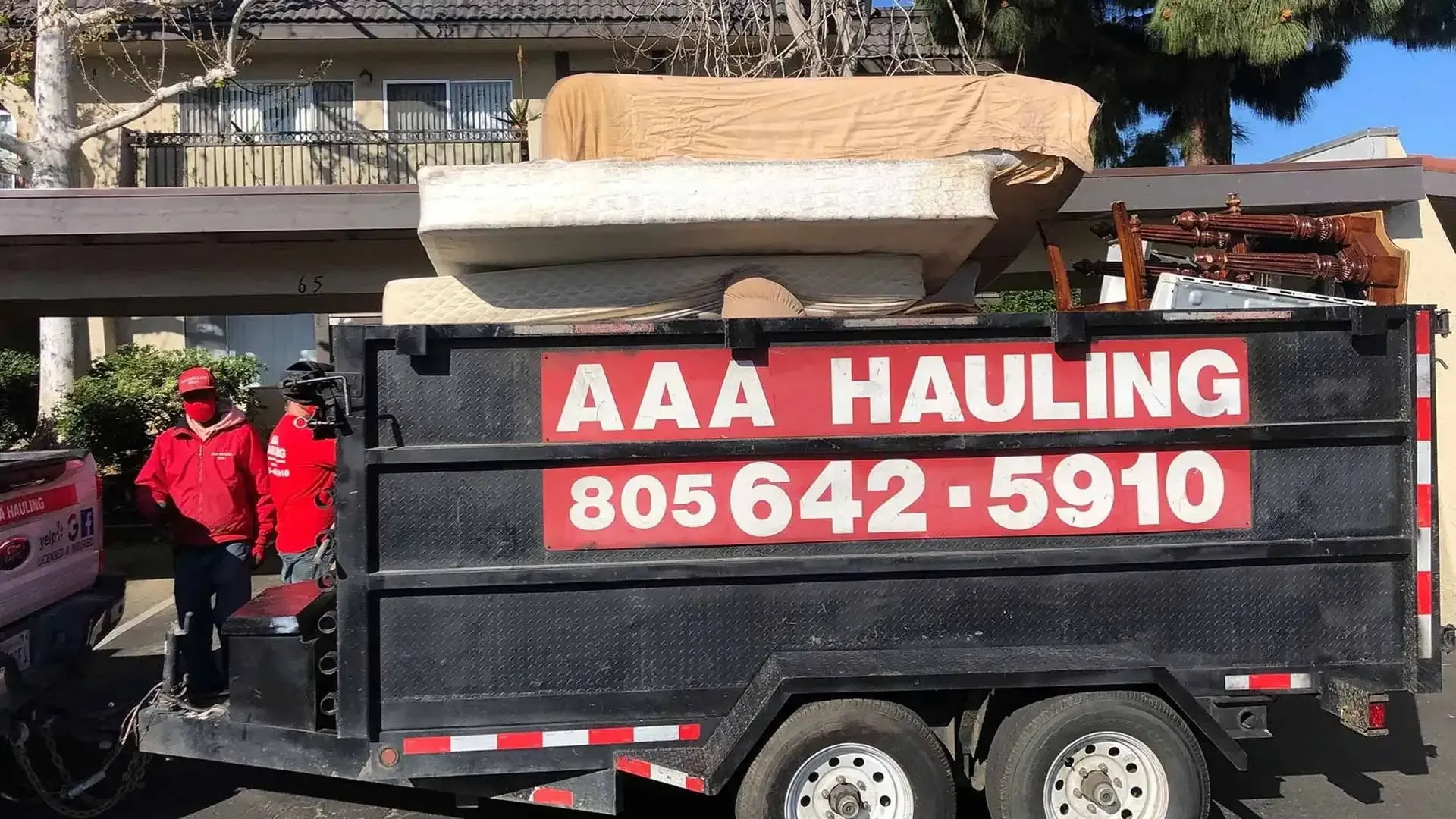 A dumpster with a mattress on top of it is parked in front of a house.