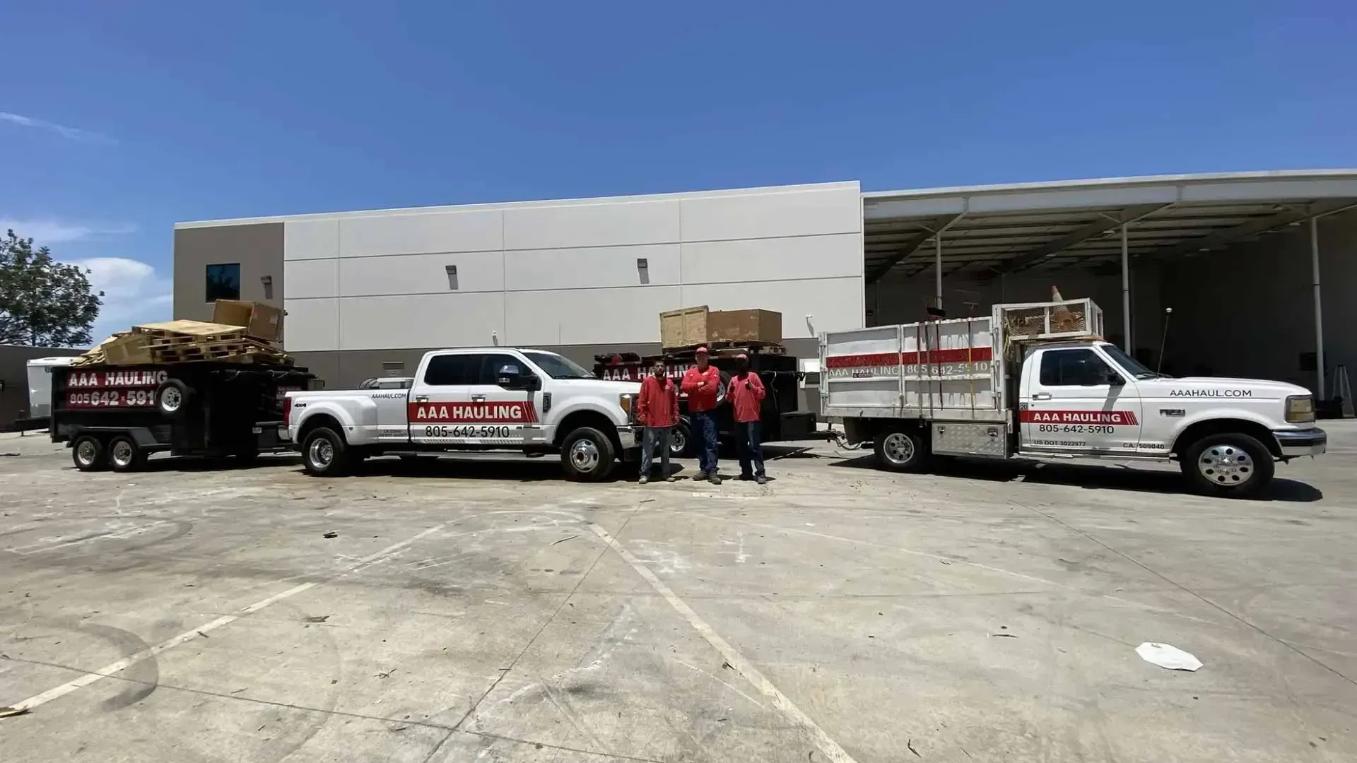 A group of trucks are parked in a parking lot in front of a building with  three people in front
