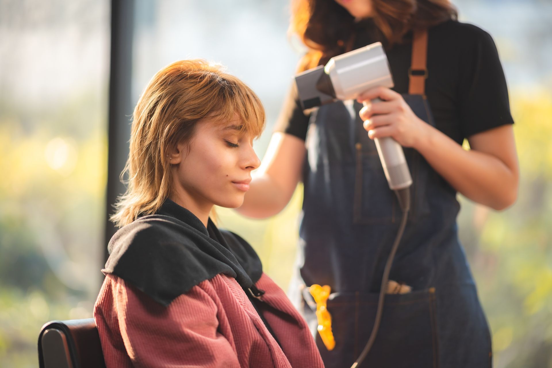 Woman having her hair dried by a hairstylist in a salon. Sunny window in background.