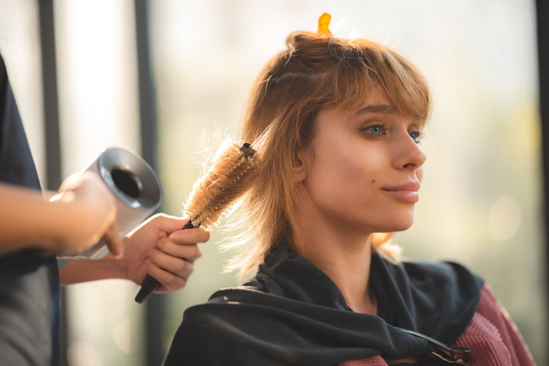 Woman getting her hair styled at a salon with a blow dryer and round brush.