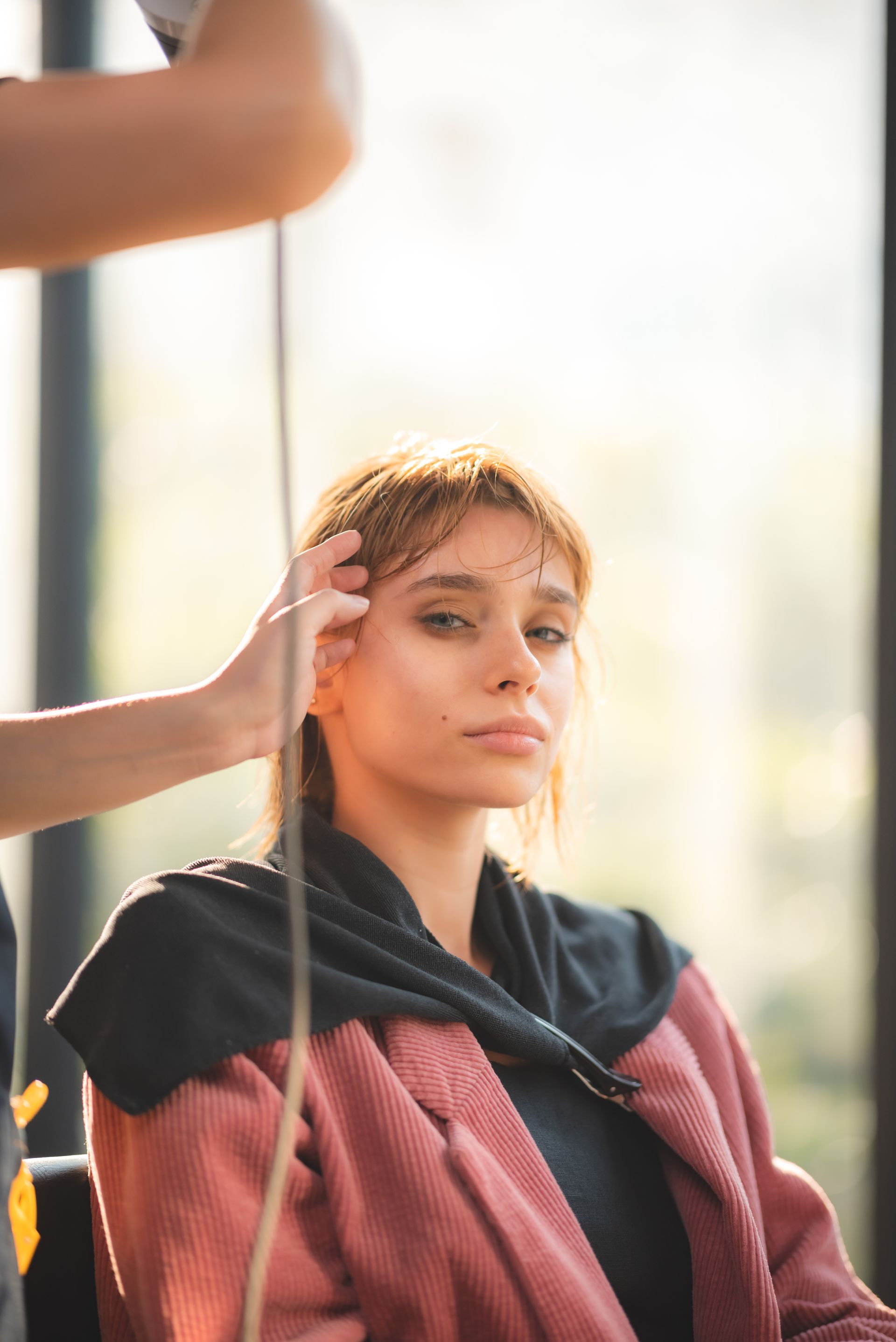 Woman at a salon, hair stylist working on her hair. Indoors, natural light.