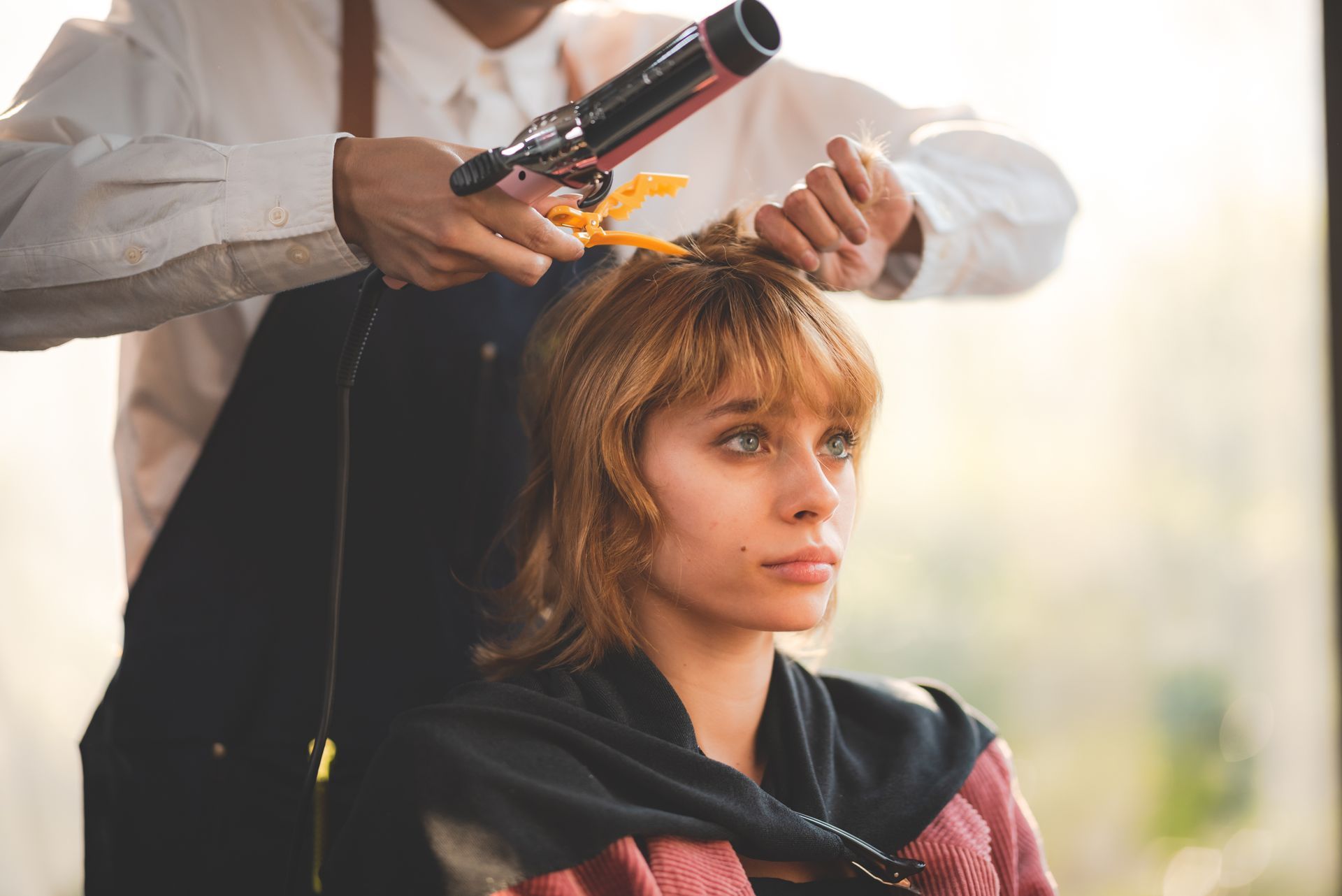 Hairdresser curling a woman's blonde hair with a curling iron in a salon, outdoors.