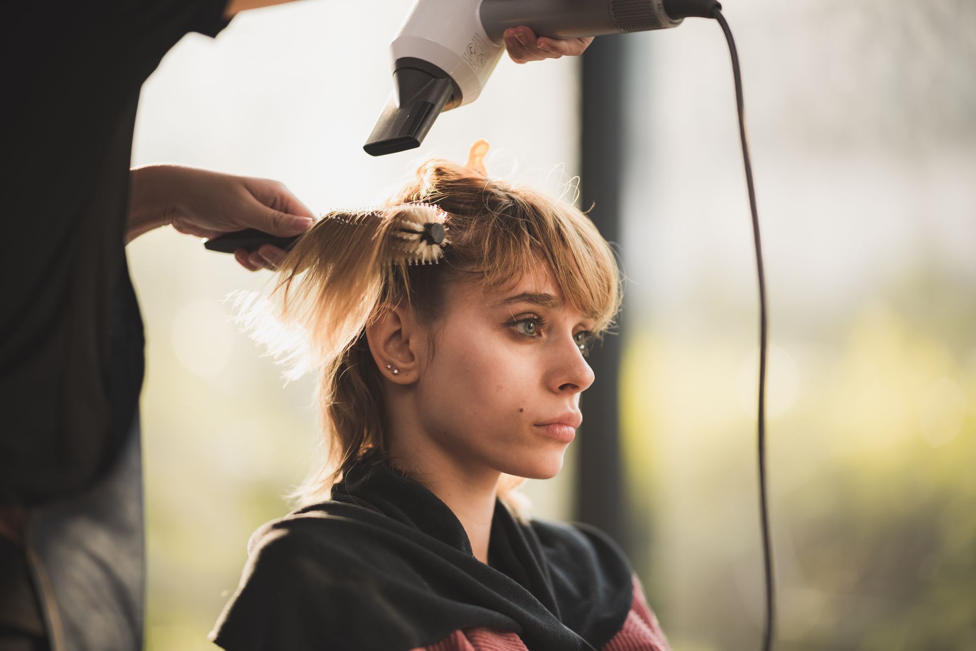 Woman getting her hair styled with a blow dryer; outdoors.