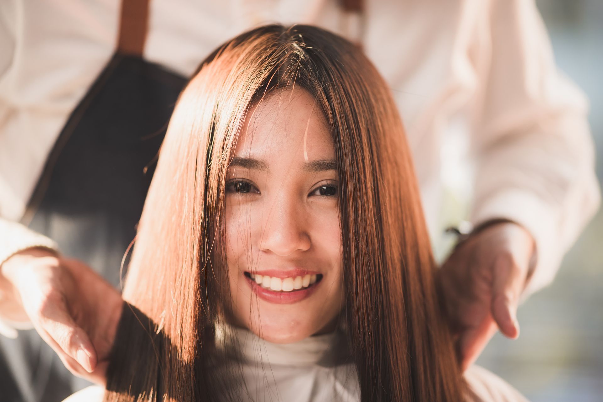 Woman with long brown hair smiles while getting hair styled.