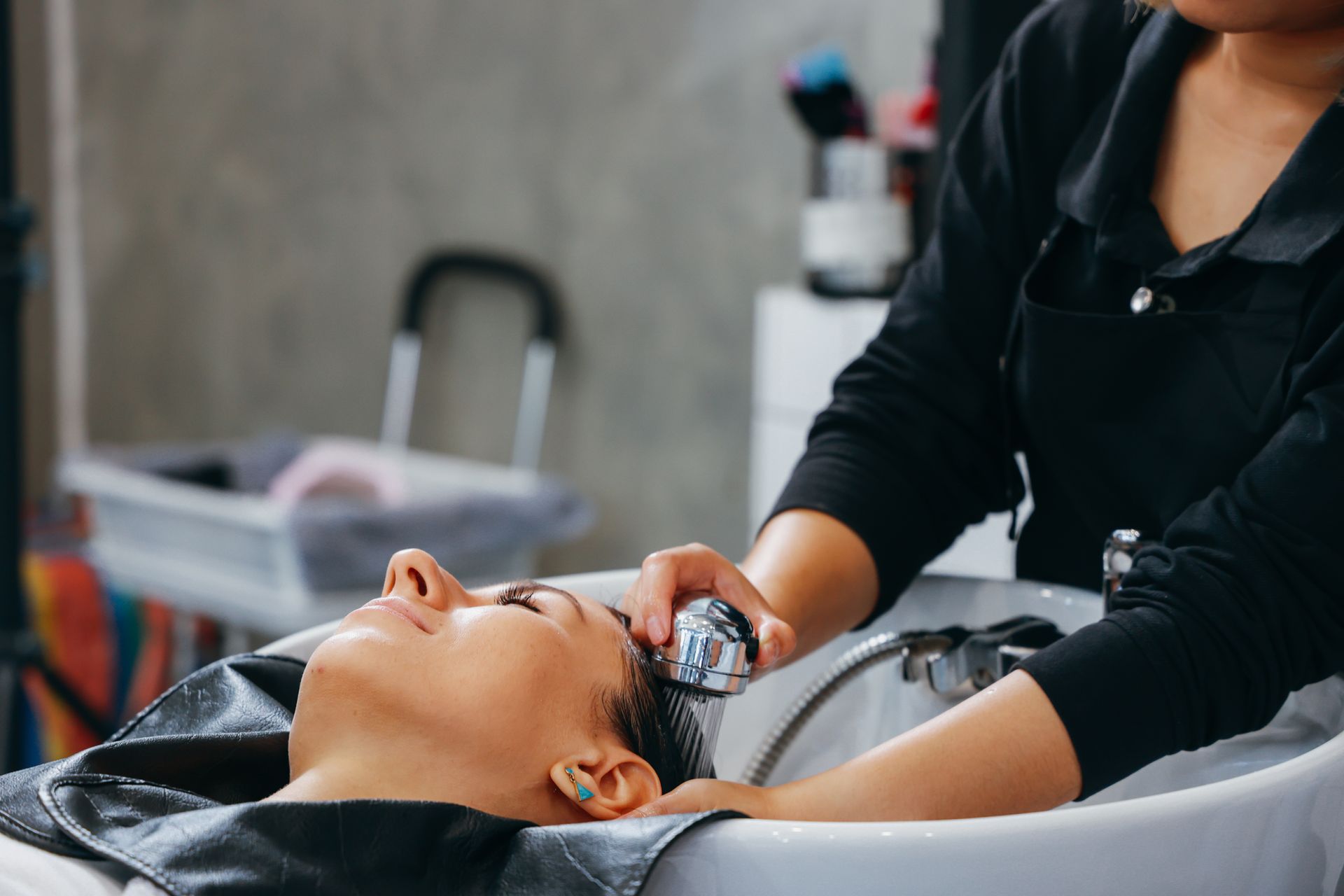 Woman getting her hair washed at a salon, head in a sink while a stylist rinses hair.