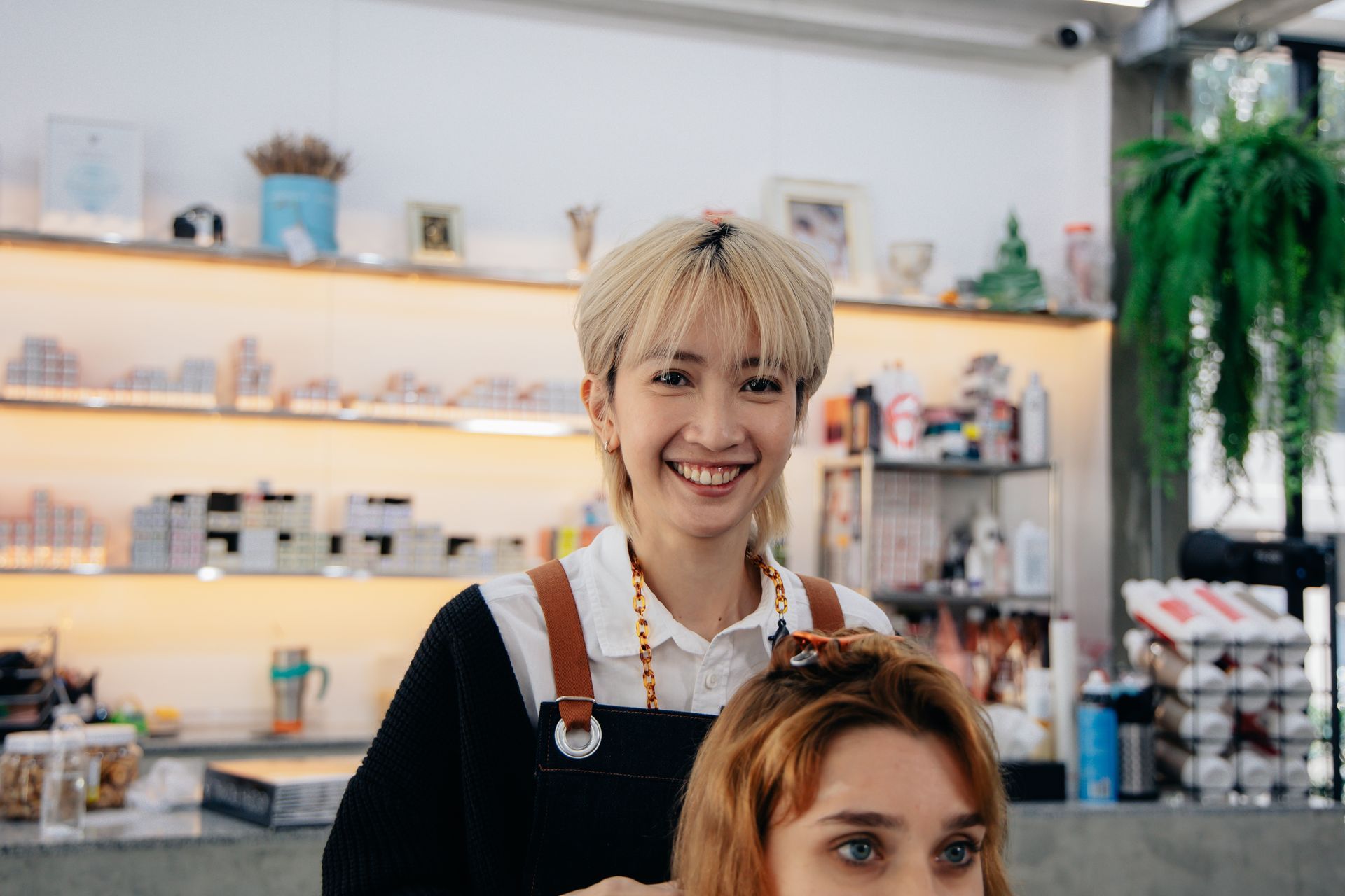 Hairdresser smiling at the camera, styling a client's hair in a salon.