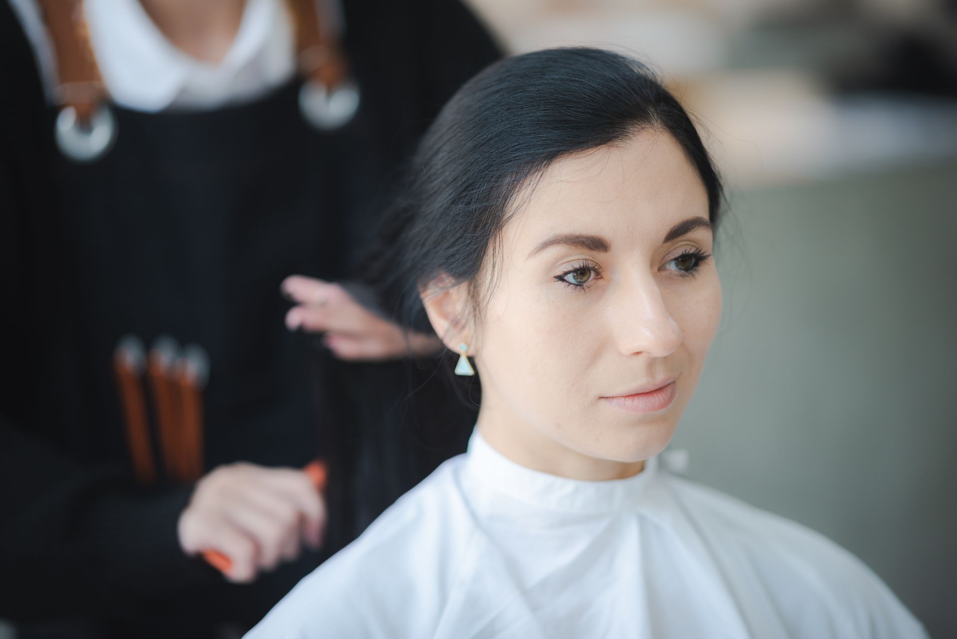 Woman getting her hair styled in a salon, wearing a white cape.