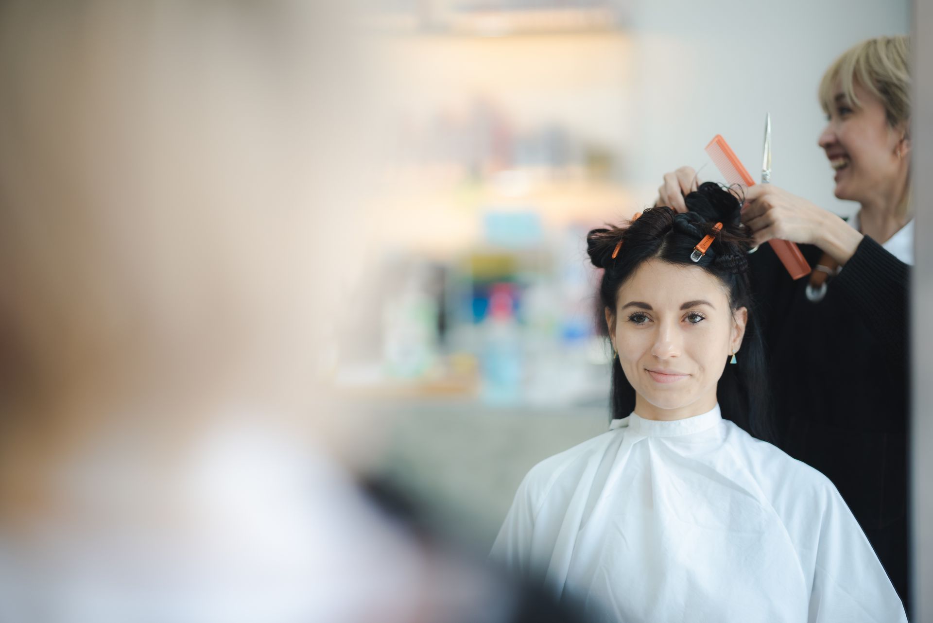 Woman getting a haircut by a smiling stylist in a salon, looking at the mirror.
